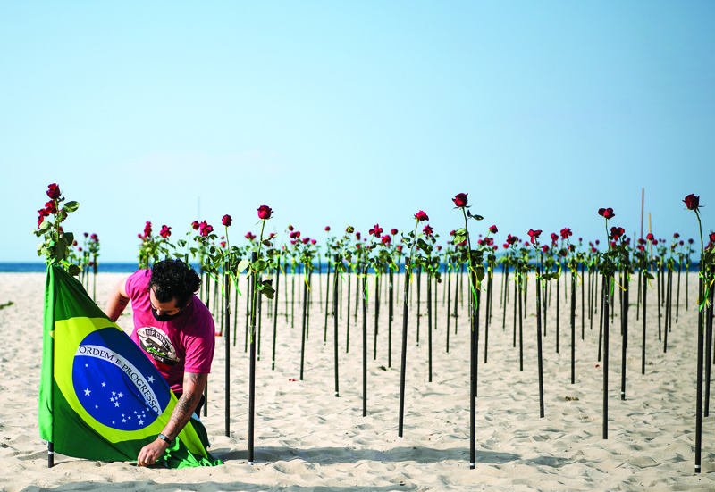 RIO DE JANEIRO: A protestor secures a Brazilian flag next to roses placed by an NGO on Copacabana beach in memory of Brazil's half a million COVID-19 victims yesterday. - AFP n