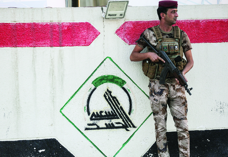 BAGHDAD: In this photo taken on June 13, 2021, a fighter of Iraq's Hashed al-Shaabi paramilitary forces stands guard next to a wall showing the group's logo outside their headquarters. - AFP n