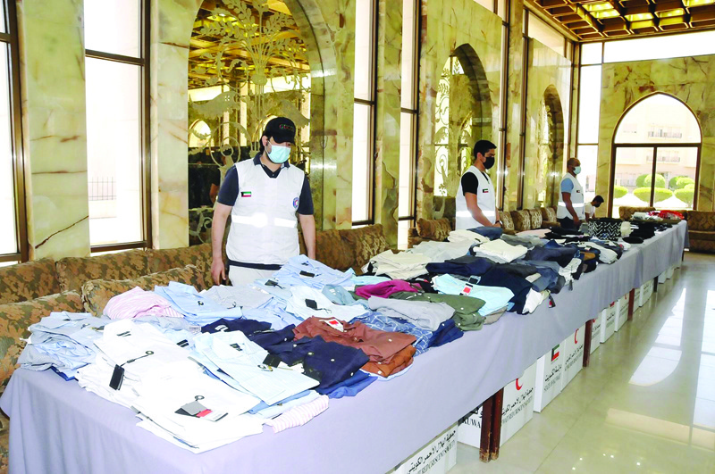 KUWAIT: KRCS workers stand next to clothes that were distributed to families in need in Kuwait. - KUNAn