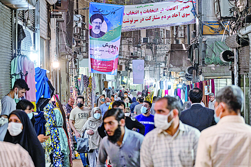 TEHRAN: Iranians walk beneath an campaign banner bearing the portrait of presidential candidate Ebrahim Raisi at the Grand Bazaar in the capital Tehran. Iran holds a presidential election today with ultraconservative Ebrahim Raisi most likely to win from the seven candidates. - AFPn