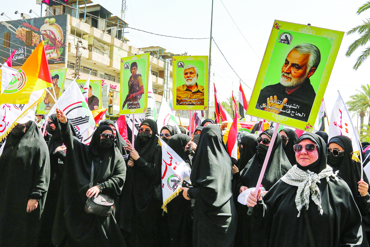 BAGHDAD: Women hold signs showing posters of (right to left) slain Iranian Revolutionary Guards commander Qasem Soleimani and Iraq's Hashed Al-Shaabi commander Abu Mahdi Al-Muhandis (both assassinated by a US drone strike in early 2020) and a slain Hashed fighter, during a symbolic funeral parade organized by the Hashed in the capital Baghdad yesterday.- AFPnn