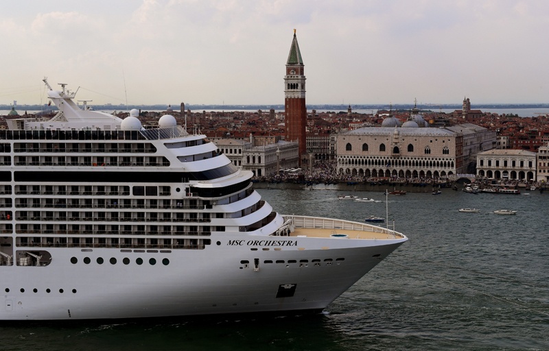 Tugboats escort the MSC Orchestra cruise ship across the basin past the Bell Tower and Doge's Palace as it leaves Venice.n