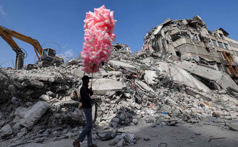 GAZA: A Palestinian peddler walks with bags of cotton candy past the rubble of a building destroyed during the May 2021 conflict between Hamas and the Zionist entity in Gaza City's Al-Rimal neighborhood on June 10, 2021. – AFP n