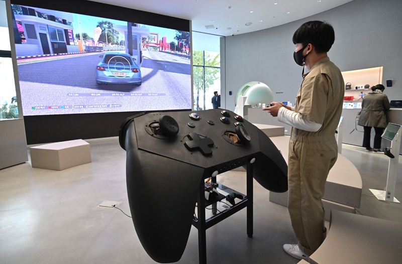 In this file photo A staff member plays a game in front of an oversized mock-up of Microsoft's Xbox controller at a flagship store of SK Telecom in Seoul . — AFP n