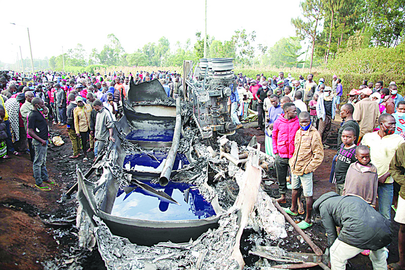 KISUMU: People stand next to a burnt out petrol tanker that burst into flames when it overturned in western Kenya, while a crowd thronged to collect the spilling fuel, on the busy highway between Kisumu and the border with Uganda, yesterday. - AFPn