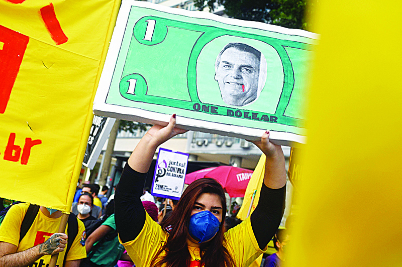 RIO DE JANEIRO: In this photo taken on July 3, 2021, a woman holds a sign depicting Brazilian President Jair Bolsonaro in a dollar bill during a protest against his handling of the COVID-19 pandemic. - AFP n