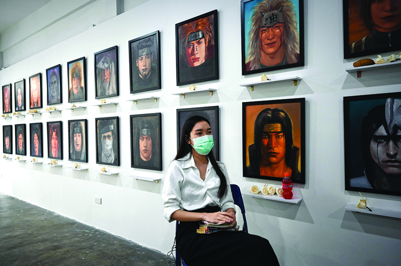Thai artist Jinnipha Nivasabut sitting with oil portraits of deceased anime characters, at her exhibition The 2D Afterlife, at Palette Artspace in Bangkok. — AFP photosn