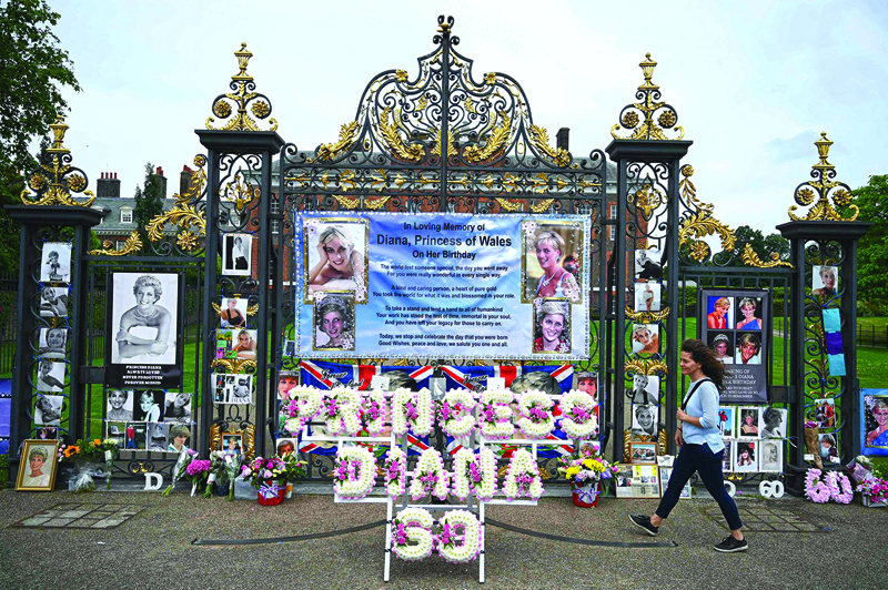Pedestrians look at wreaths and pictures attached to the gates of Kensington Palace to celebrate what would have been Princess Diana's 60th birthday in London yesterday. - AFPn