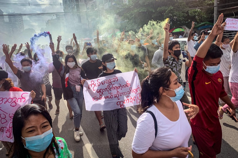 Protesters make the three-finger salute and hold flares during a demonstration against the military coup in Yangon on July 3, 2021. - AFP)