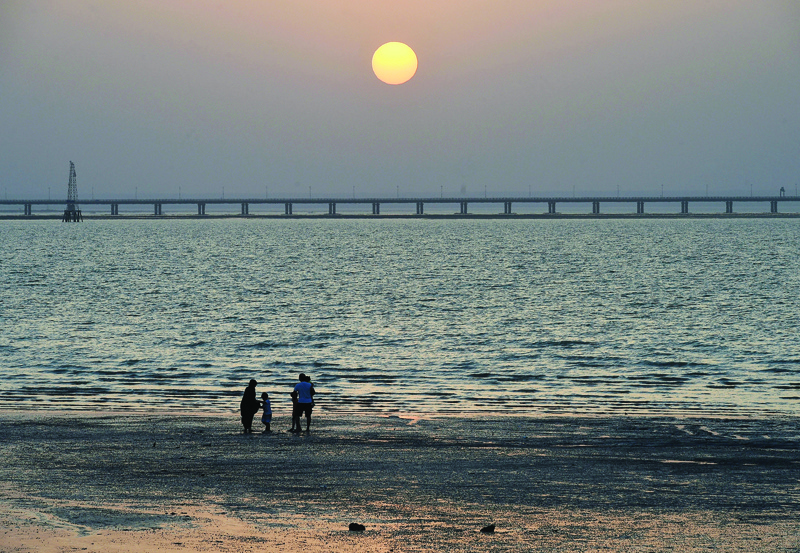 KUWAIT: A family is seen at Shuwaikh Beach as the sun sets behind Jaber Causeway on Friday. - Xinhuan