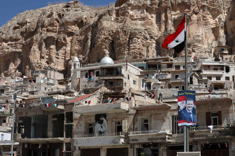 A national flag and portraits of Syrian President Bashar al-Assad are pictured in the village of Maalula north of the Syrian capital Damascus. — AFP photosn