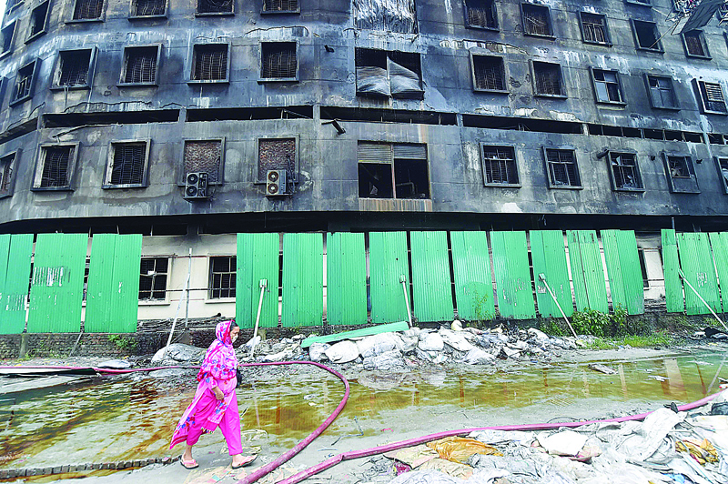 RUPGANJ, Bangladesh: A garment worker walks past the burnt factory after a fire was put out on Saturday. - AFP  n