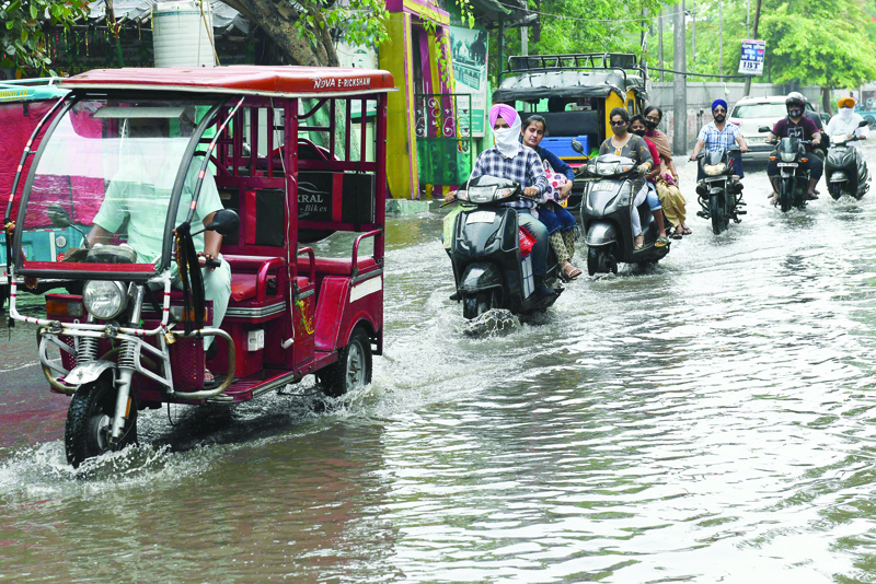 AMRITSAR: Commuters make their way through a water-logged street after a rain shower in Amritsar yesterday. - AFPn