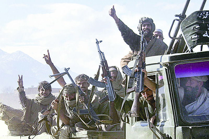 (Left) This file photo taken on Dec 23, 2001 shows Afghan anti-Taleban fighters flashing the victory sign as they leave the Tora Bora mountain area to make their way to their base. (Right) This file photo taken on Dec 16, 2001 shows US Defense Secretary Donald Rumsfeld throwing up his arms as he concludes his town hall meeting with US troops at Bagram airfield after he met Afghanistan's new leaders to discuss the country's future. - AFP photos n