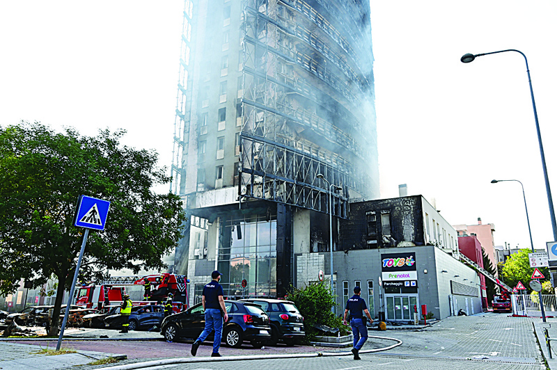 MILAN: Policemen walk by a 20-storey residential building which caught fire the day before yesterday in Milan. - AFPn