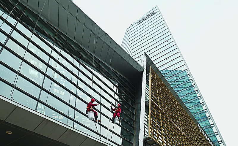 BEIJING: Workers clean the glass facade of a mall in Beijing yesterday.-AFPn