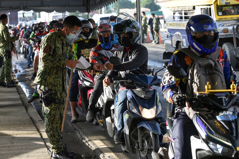This photo taken on August 6, 2021 shows a policeman checking motorists' documents as they cross from nearby Rizal province into Metro Manila, at a provincial border checkpoint in Quezon City, suburban Manila. - AFPn