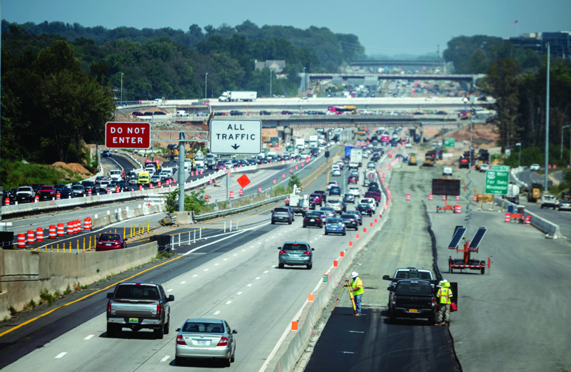 FAIRFAX, US: Cars drive past construction workers along Interstate Highway 66 in Fairfax, Virginia, yesterday.-AFPn