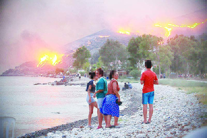 MILAS, Turkey: People on a beach watch blazes spreading up a hill in the Aegean coast city of Oren in the holiday region of Mugla on Tuesday. - AFP n