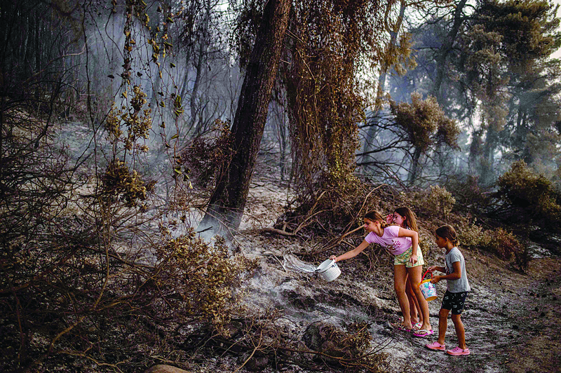 AYII, Greece: Children pour water after a forest fire near the village of Kastri on Evia island on Tuesday. – AFP n