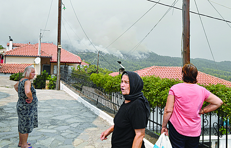 KOURKOULI, Greece: Residents react as they watch smoke rising from a hill by the village of Kourkouli, North Evia, yesterday as Greek firefighters battled to bring under control two major fires raging near Olympia and on the island of Evia as the country swelters in a record-breaking heatwave. - AFPnn