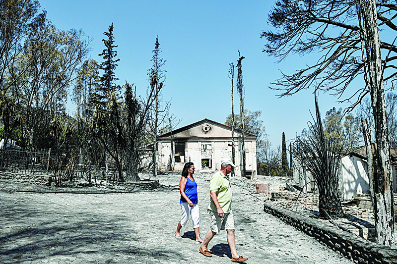 LABIRI: Locals walk past burnt buildings at the seaside resort of Labiri (Lambiri) east of the city of Patras Sunday. — AFPn