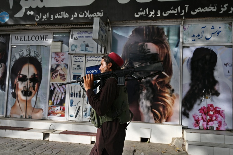 KABUL: A Taleban fighter walks past a beauty salon with images of women defaced using spray paint in Shar-e-Naw yesterday. – AFP n