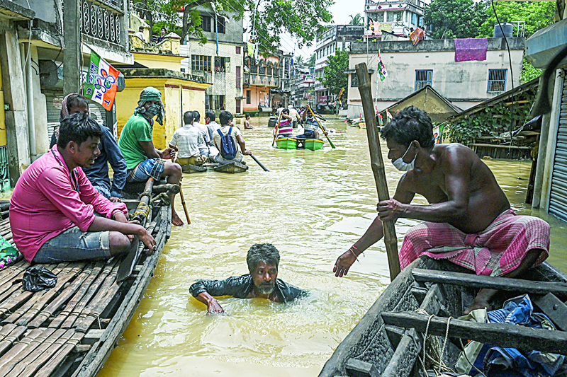 KOLKATA: A resident (right) sitting on a boat helps a man (center) walking through a road submerged by floodwaters following heavy monsoon rains in Ghatal, Paschim Medinipur district, about 100 km from Kolkata Monday.  - AFPnn