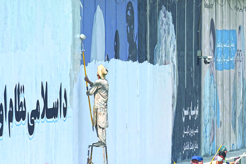A man paints over murals on a concrete wall along a street in Kabul.—AFP photosn