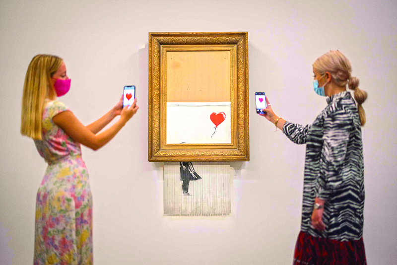 Assistants pose by an artwork titled ‘Love is the Bin’ by British street artist Banksy during a photocall at Sotheby’s auction house in central London.—AFP n
