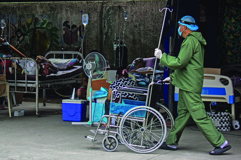 BINAN: A nurse wearing a personal protective suit walks past suspected COVID-19 patients resting in a parking lot turned into a COVID ward outside a hospital in Binan town, Laguna province south of Manila yesterday.- AFP n