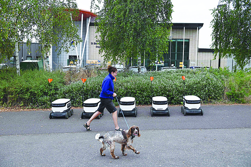 MILTON KEYNES: A pedestrian walks her dog next to a line of parked autonomous robots called Starship before delivering groceries from a nearby Co-op supermarket in Milton Keynes, England. - AFP n