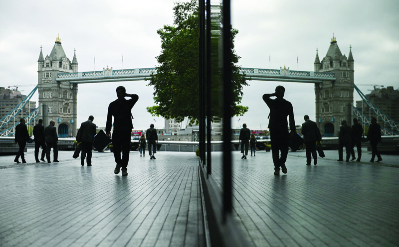 LONDON: Pedestrians are reflected in the window of a building as they walk near Tower Bridge in London yesterday.-AFPn
