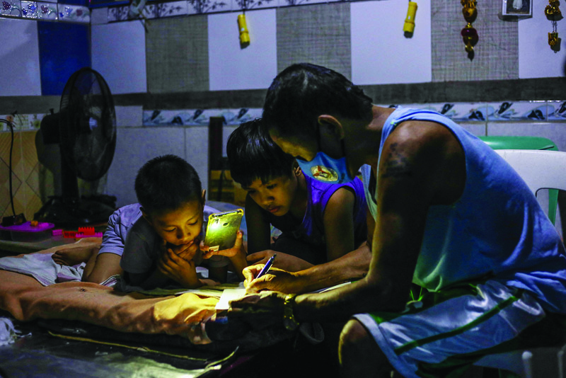 MANILA:  Petronilo Pacayra Sr signs school documents while his children (aged nine and ten) look on at their home in Quezon City, suburban Manila.- AFP n