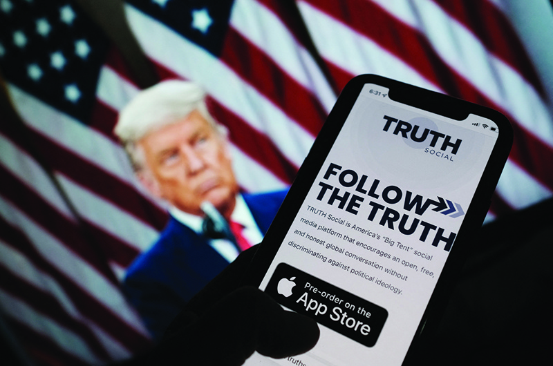 LOS ANGELES: A person checks the app store on a smartphone for 'Truth Social,' with a photo of former US President Donald Trump on a computer screen in the background. - AFP