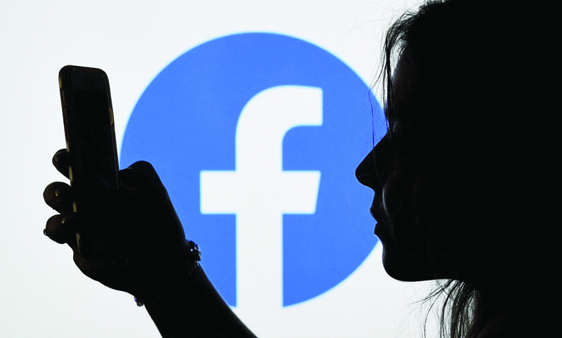 ARLINGTON: A person looks at a smart phone with a Facebook App logo displayed on the background,  in Arlington, Virginia. - AFP n