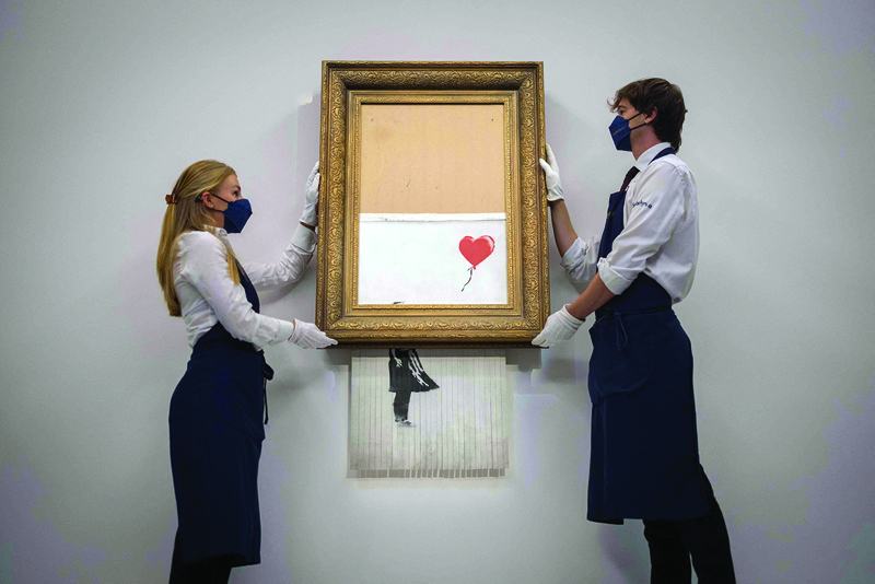 In this file photo assistants pose alongside an artwork titled 'Love is the Bin' by British street artist Banksy during a photocall at Sotheby's auction house in central London.-AFP n