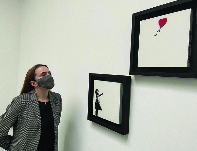 A gallery employee poses with an artwork entitled ‘Girl and Balloon’ (Diptych) by Banksy, during a photocall at Christie’s auction house in central London.—AFP n