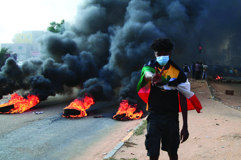 KHARTOUM: A Sudanese protester draped with the national flag flashes the victory sign next to burning tires during a demonstration yesterday. - AFP n