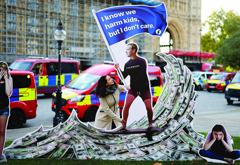 LONDON: A demonstrator poses with an installation depicting Facebook founder Mark Zuckerberg surfing on a wave of cash and surrounded by distressed teenagers during a protest opposite the Houses of Parliament yesterday. - AFP n
