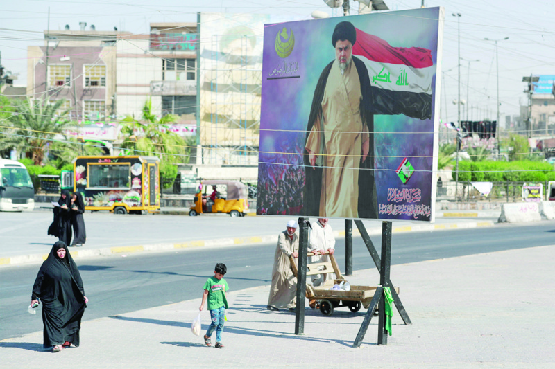 BAGHDAD: Iraqis pass by a poster of Shiite cleric Muqtada Al-Sadr in Sadr City in Baghdad, where the Sadrist movement has made remarkable progress. - AFP n