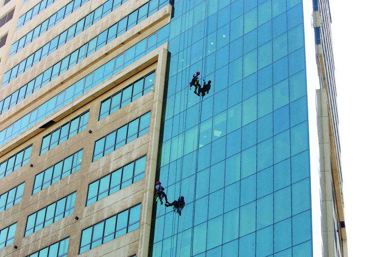 Workers clean the windows of a building in Kuwait City on November 4, 2021. - Photo by Yasser Al-Zayyatn