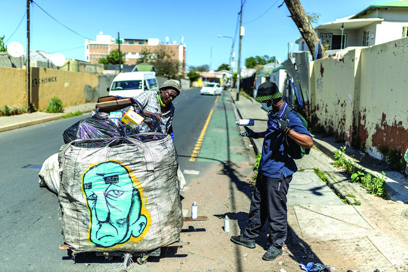 A reclaimer (left) packs his trolley full of waste after uNathi Nzina), a graffiti artist, sprayed it, as part of an initiative to make their graffiti art mobile and make reclaimers more visible and identifiable, in Johannesburg.-AFP n