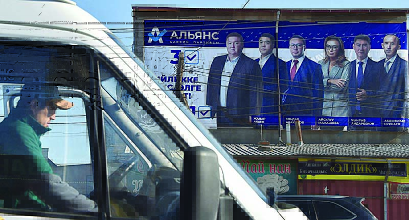 BISHKEK: A man sits in a car near a campaign poster of candidates in the upcoming parliamentary election in Bishkek.  - AFPnn