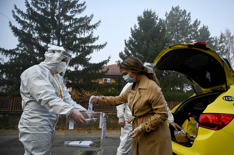 SOFIA: An electoral staff member of a mobile polling center, wearing Personal Protective Equipment (PPE), presents a ballot box to a woman in self-quarantine to collect her vote for the second-round of the presidential election and the parliamentary elections. – AFPnn