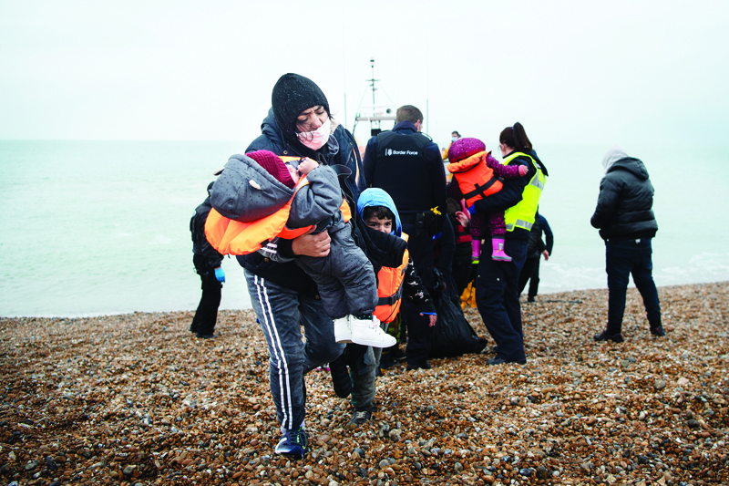 DUNGENESS, UK: A migrant carries her children after being helped ashore from a RNLI (Royal National Lifeboat Institution) lifeboat at a beach in Dungeness, on the south-east coast of England, on Wednesday after being rescued while crossing the English Channel. --AFPnn