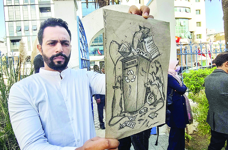TUNIS: Maamoun Ajmi, a 29-year-old architect, displays a caricature during a sit in on Nov 11, 2021 to express solidarity with the town of Agareb over the reopening of a rubbish dump. — AFP