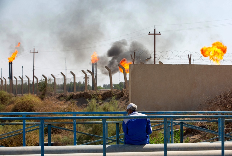 A man sits across flare stacks burning off excess gas at the Nahr Bin Omar oilfield in Iraq's southern province of Basra on Oct 25, 2021. – AFP n