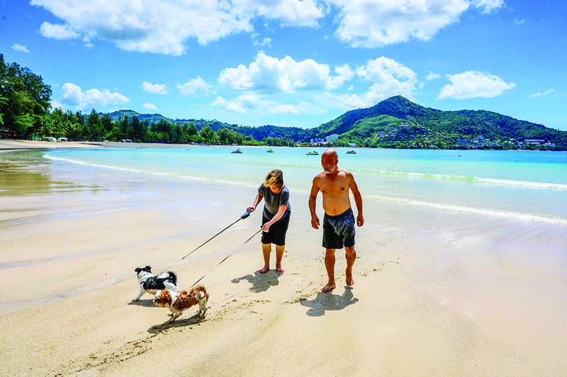 PHUKET: Tourists walk their dogs on a beach yesterday. - AFP n