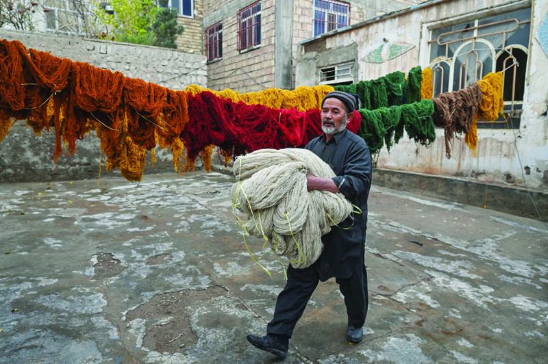 HERAT, Afghanistan: A worker walks while holding bundles wool while making carpets in Herat.  - AFPn
